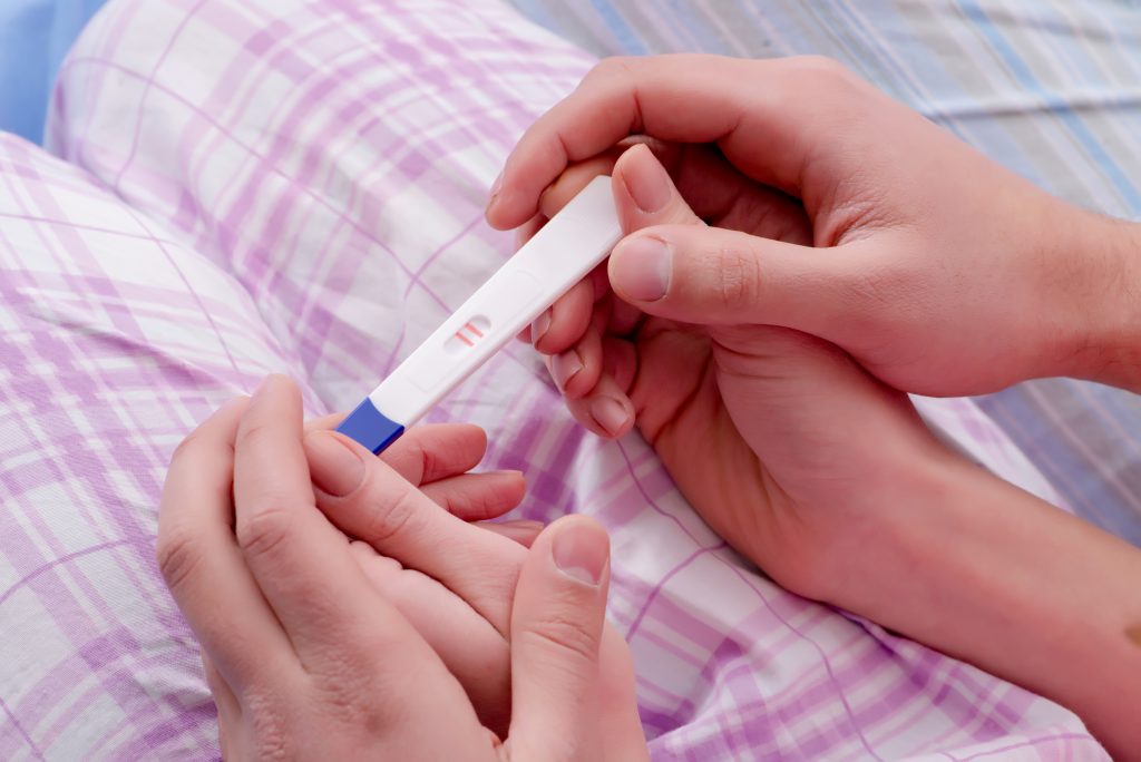 Mannen- en vrouwenhand houden positieve zwangerschapstest vast.