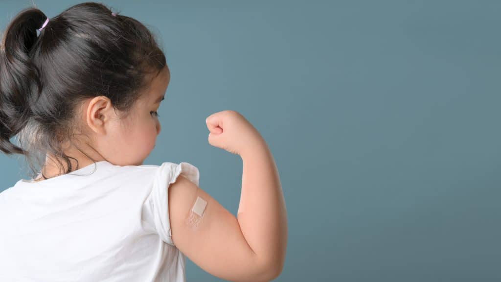 Jong meisje laat spierbal zien met pleister op de arm waar de vaccinatie is gezet.